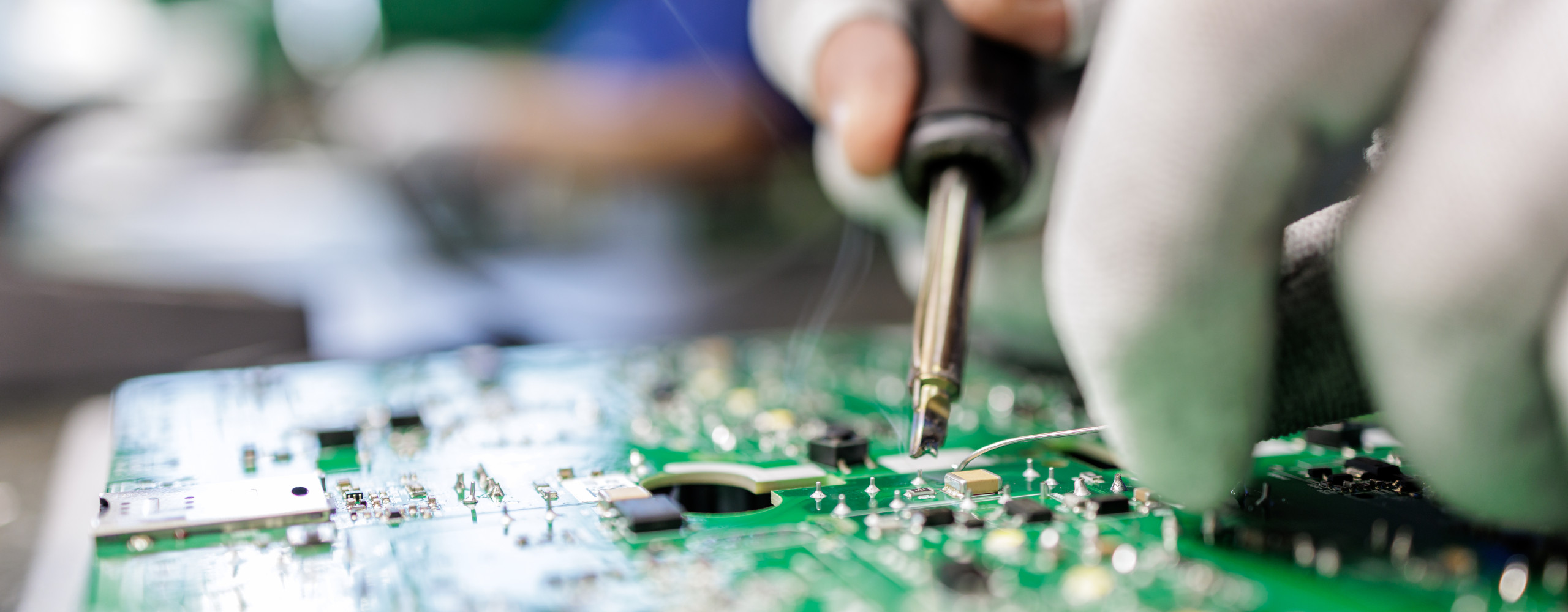 An einer elektronischen Platine werden manuell kleine Reparaturen mittels Löten durchgeführt.